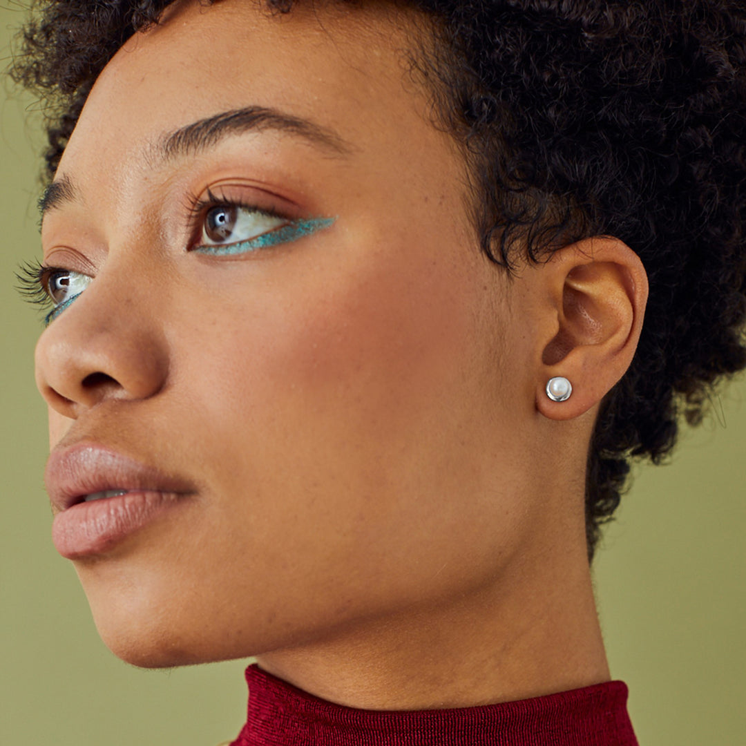 Close-up of model wearing silver pearl stud earrings on a green background