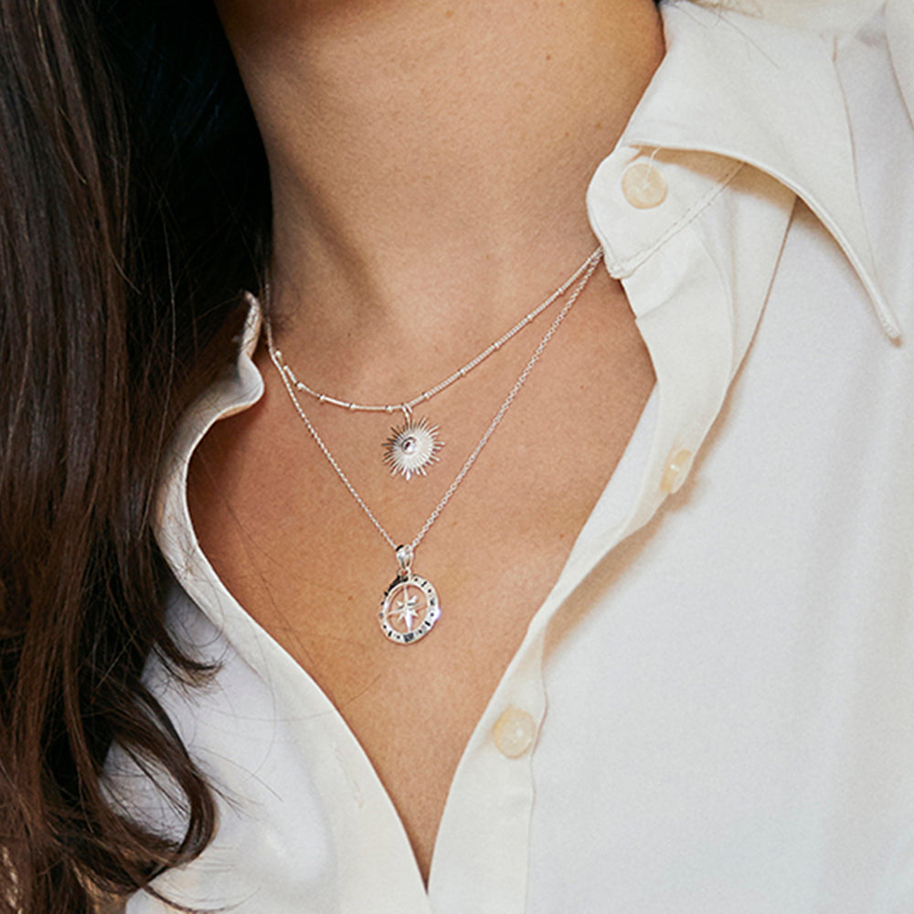 Close-up of model wearing silver compass and sun necklaces with a white shirt