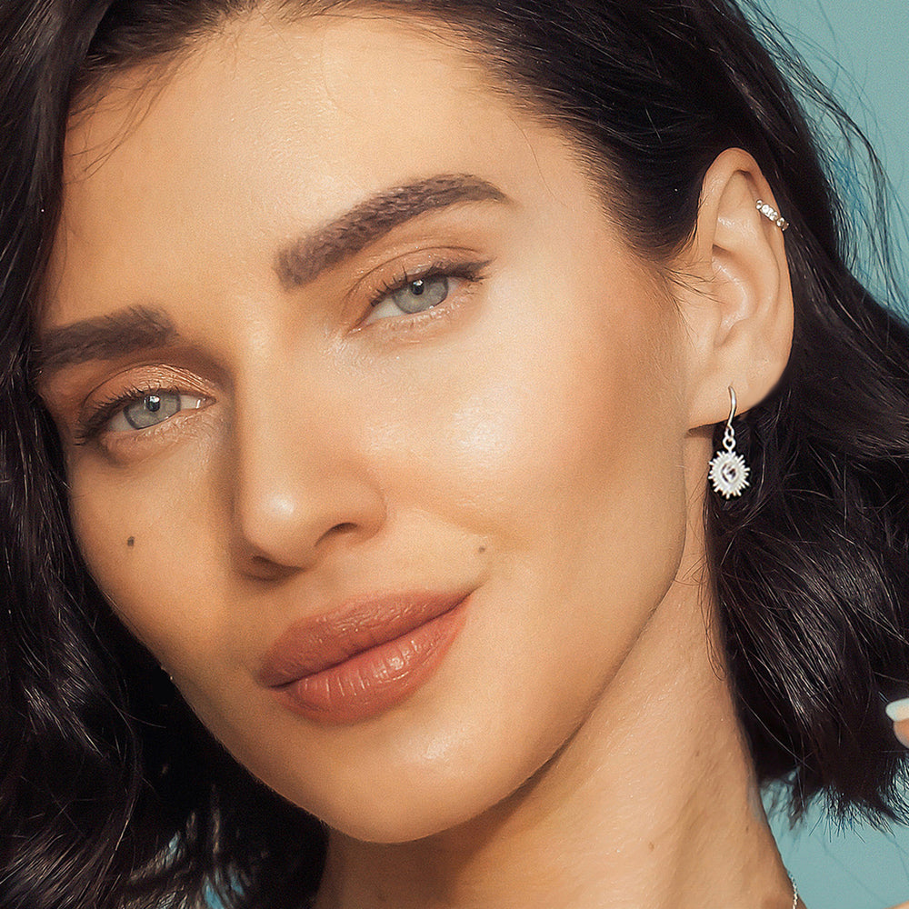 Close-up of model wearing dainty silver sun earrings set with white topaz