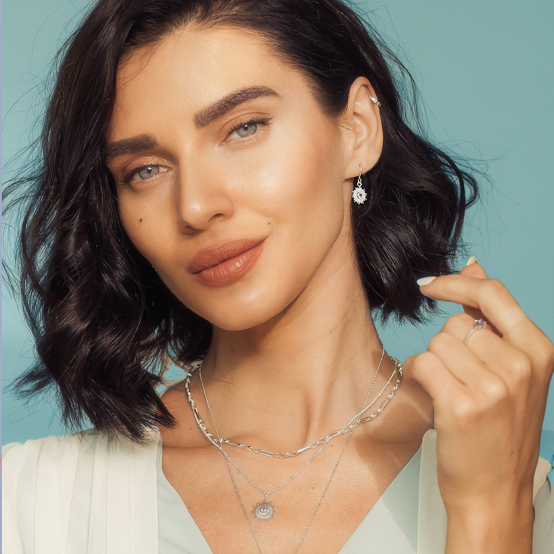 Model wearing a silver sun necklace and earring set with white topaz gems.