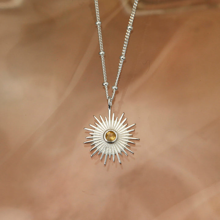 silver sun pendant in silver with a faceted citrine gemstone on a brown background