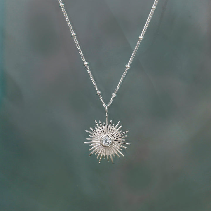 Silver sun topaz necklace with a beaded curb chain necklace on a gray background