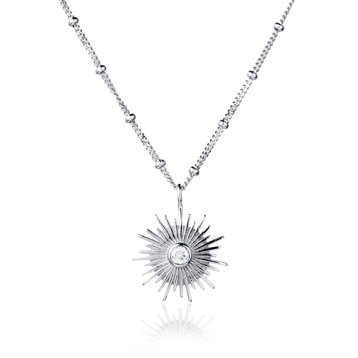 Silver sun necklace with a white topaz gemstone on a beaded curb chain on white background