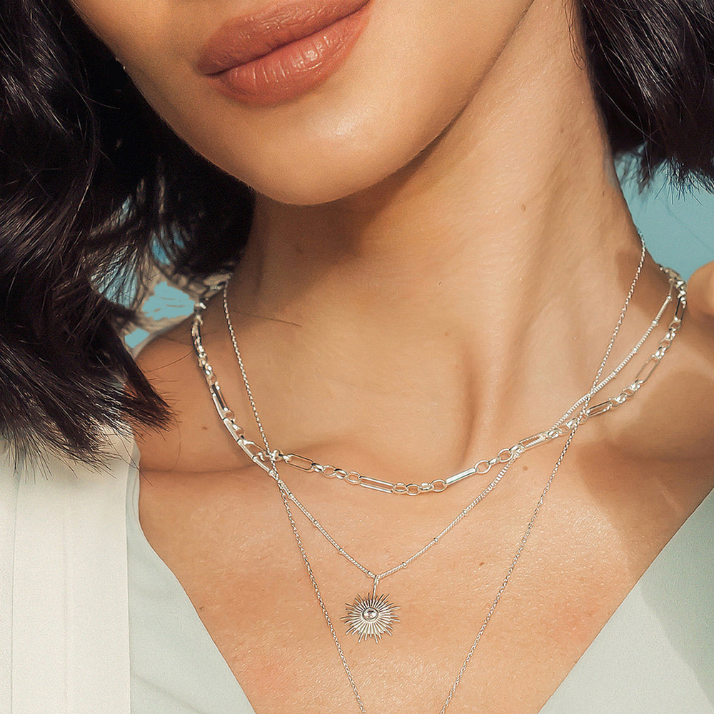 Close up of model wearing a silver sun necklace with chains and a white gemstone.