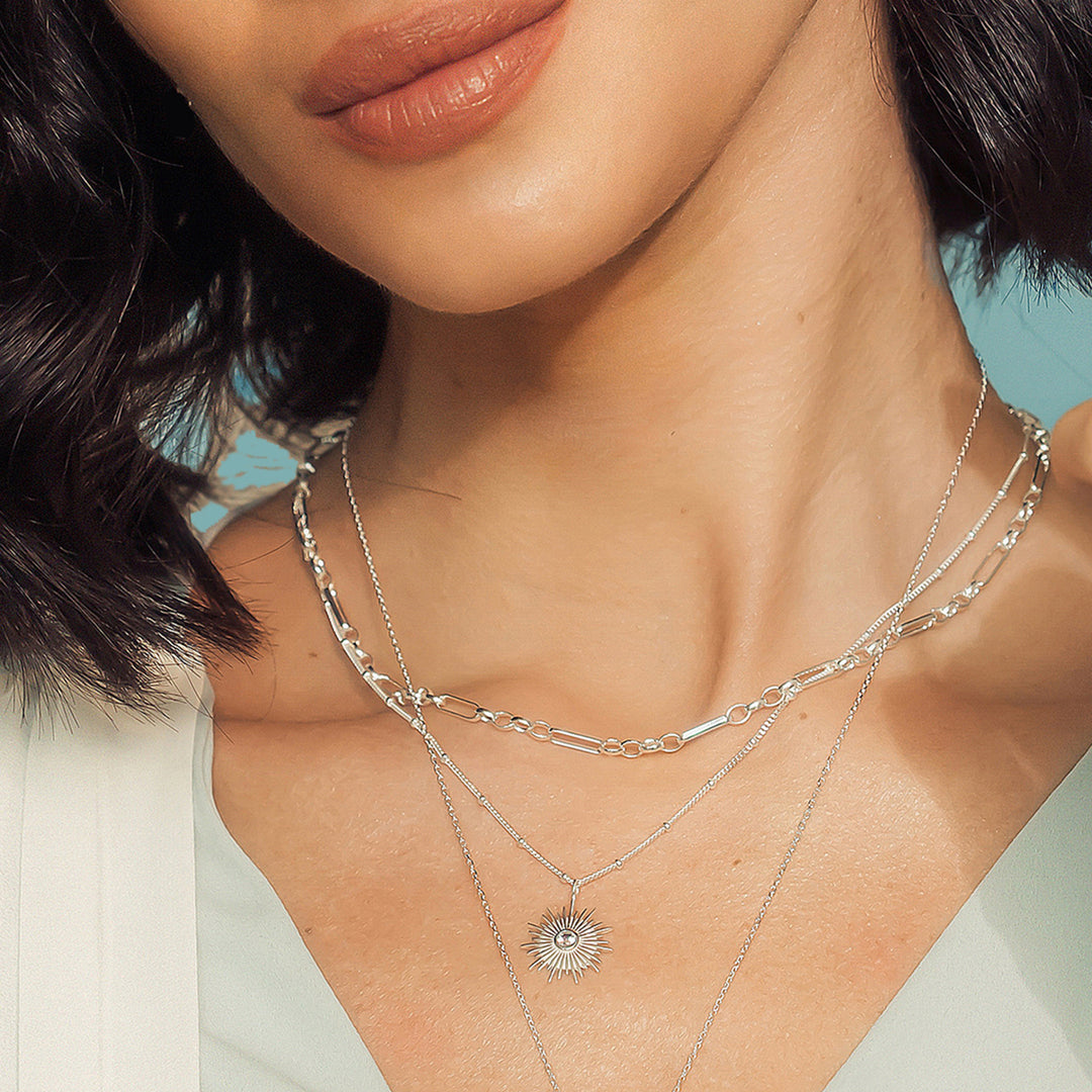 Close up of model wearing a silver sun necklace with chains and a white gemstone.