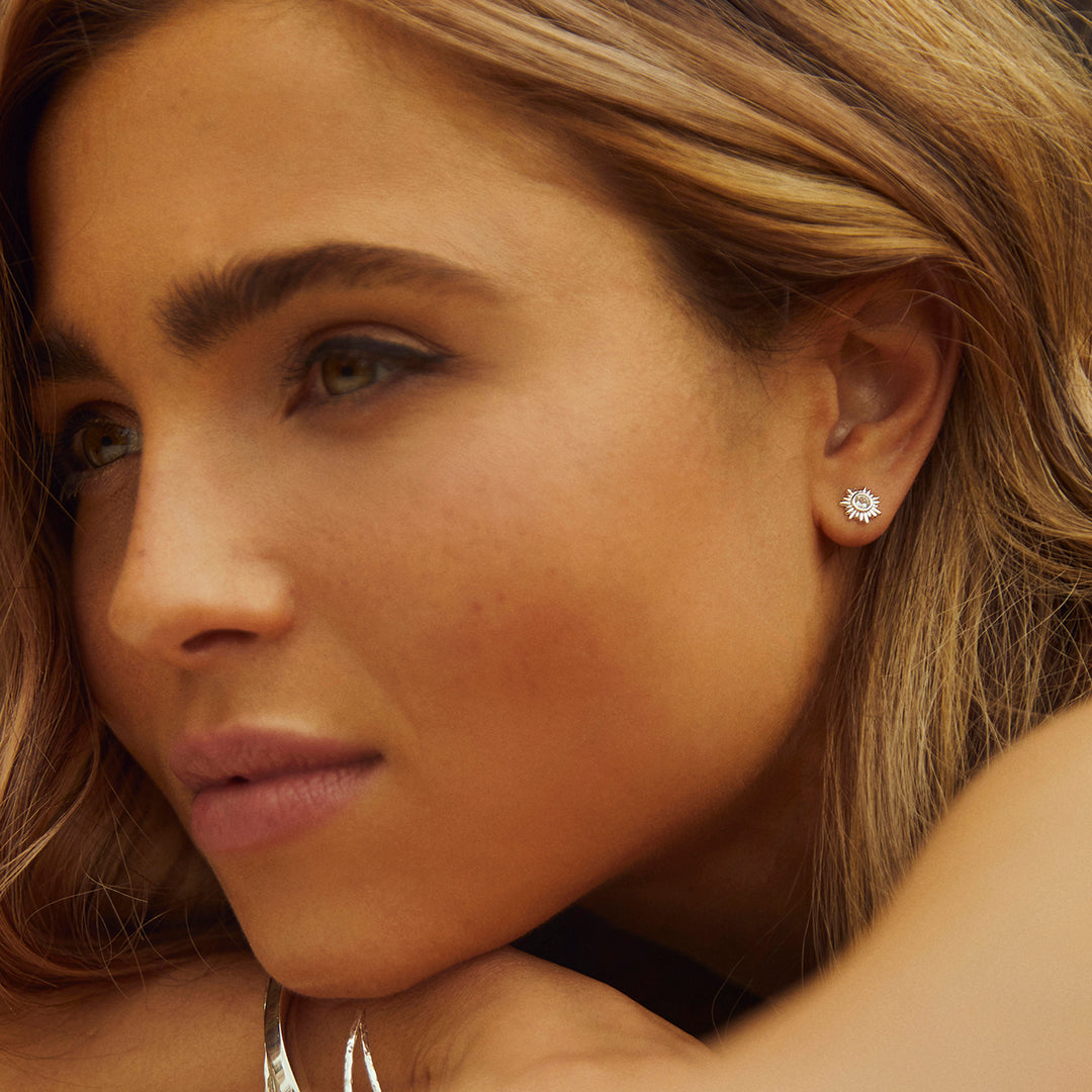 Close-up  of model wearing silver sun post earrings with faceted white topaz