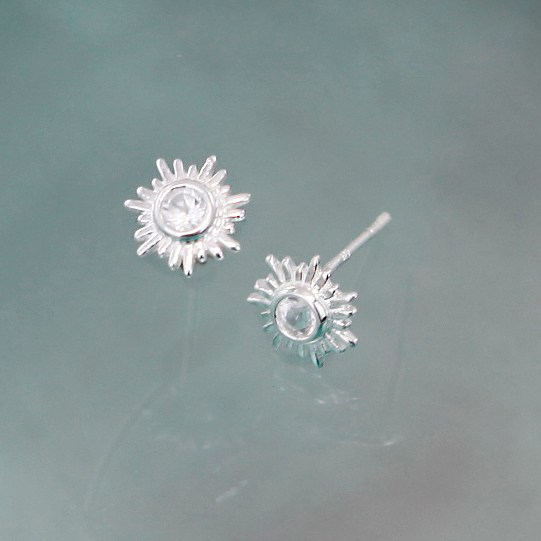 Silver stud earring in a sun design with topaz gemstones on a gray background.