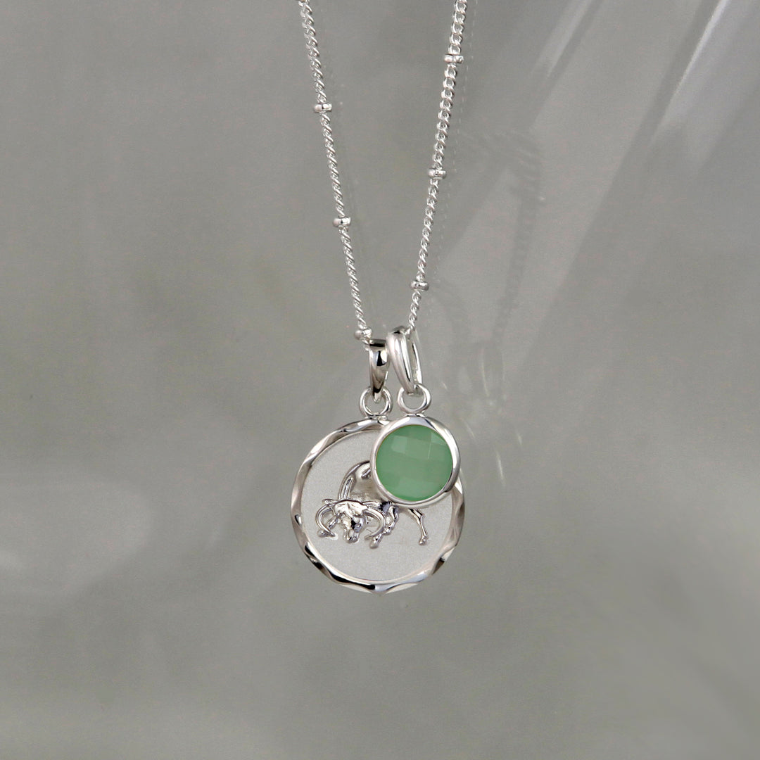 Silver Taurus Zodiac Pendant with a green quartz may birthstone charm on a gray background