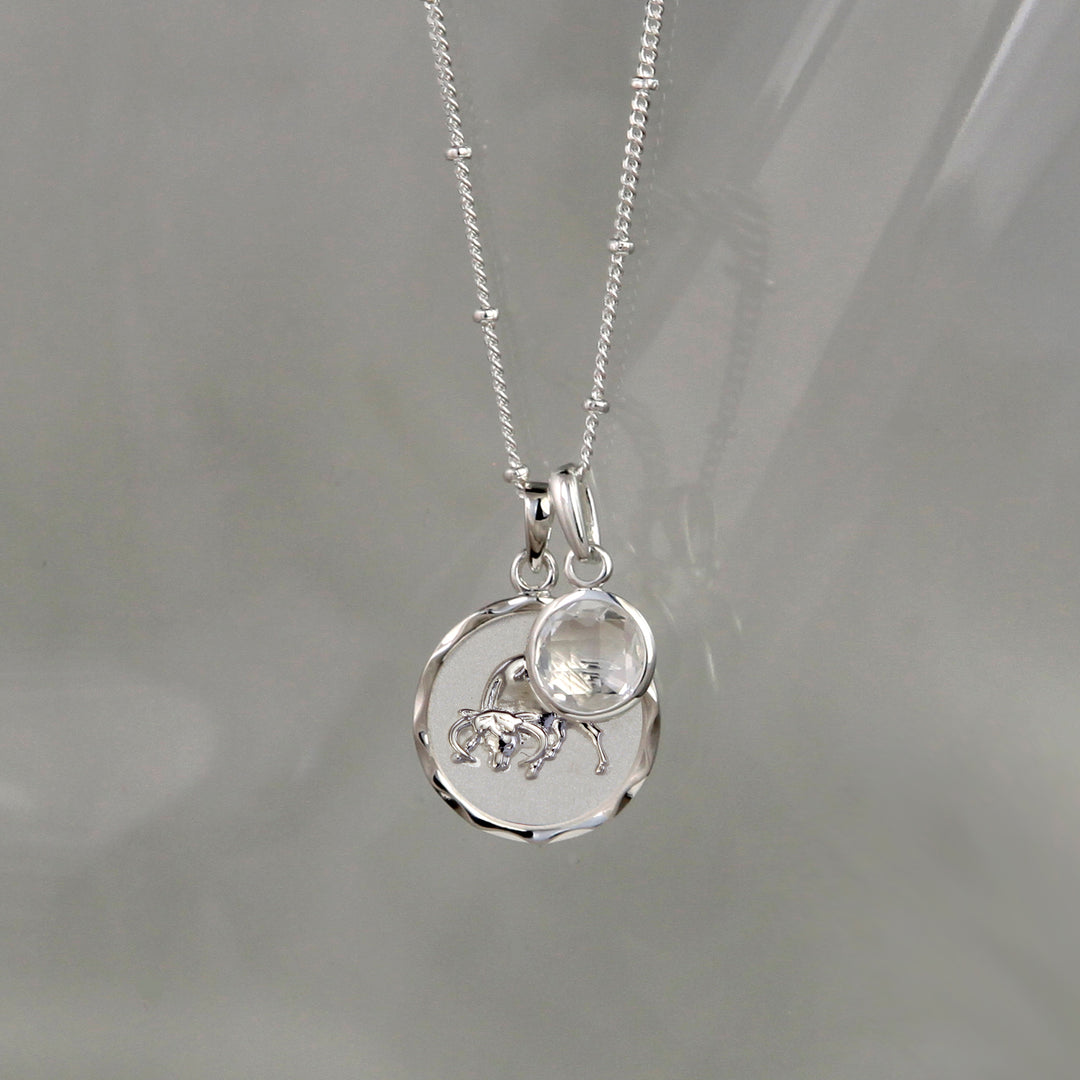 Silver Taurus Zodiac Pendant with a white topaz April birthstone charm on a gray background