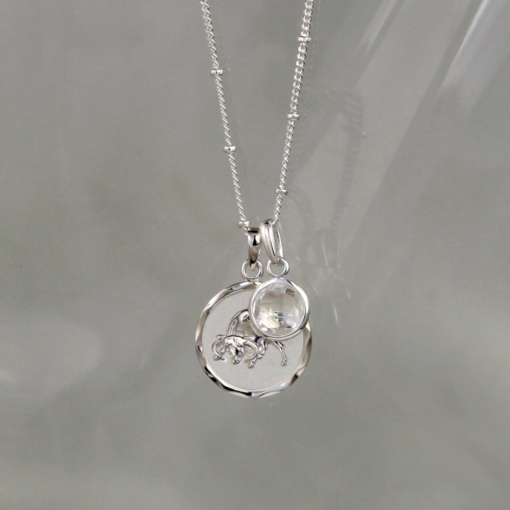 Silver Taurus Zodiac Pendant with a white topaz April birthstone charm on a gray background