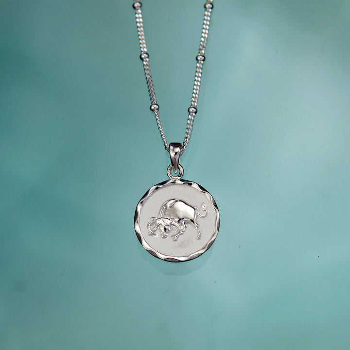 Silver Taurus star sign necklace on an aqua background