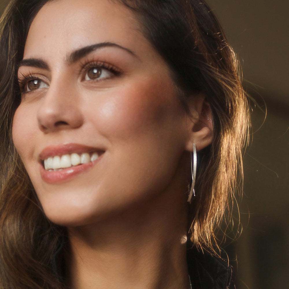 Close-up of a woman with silver threader earrings against a blurred background