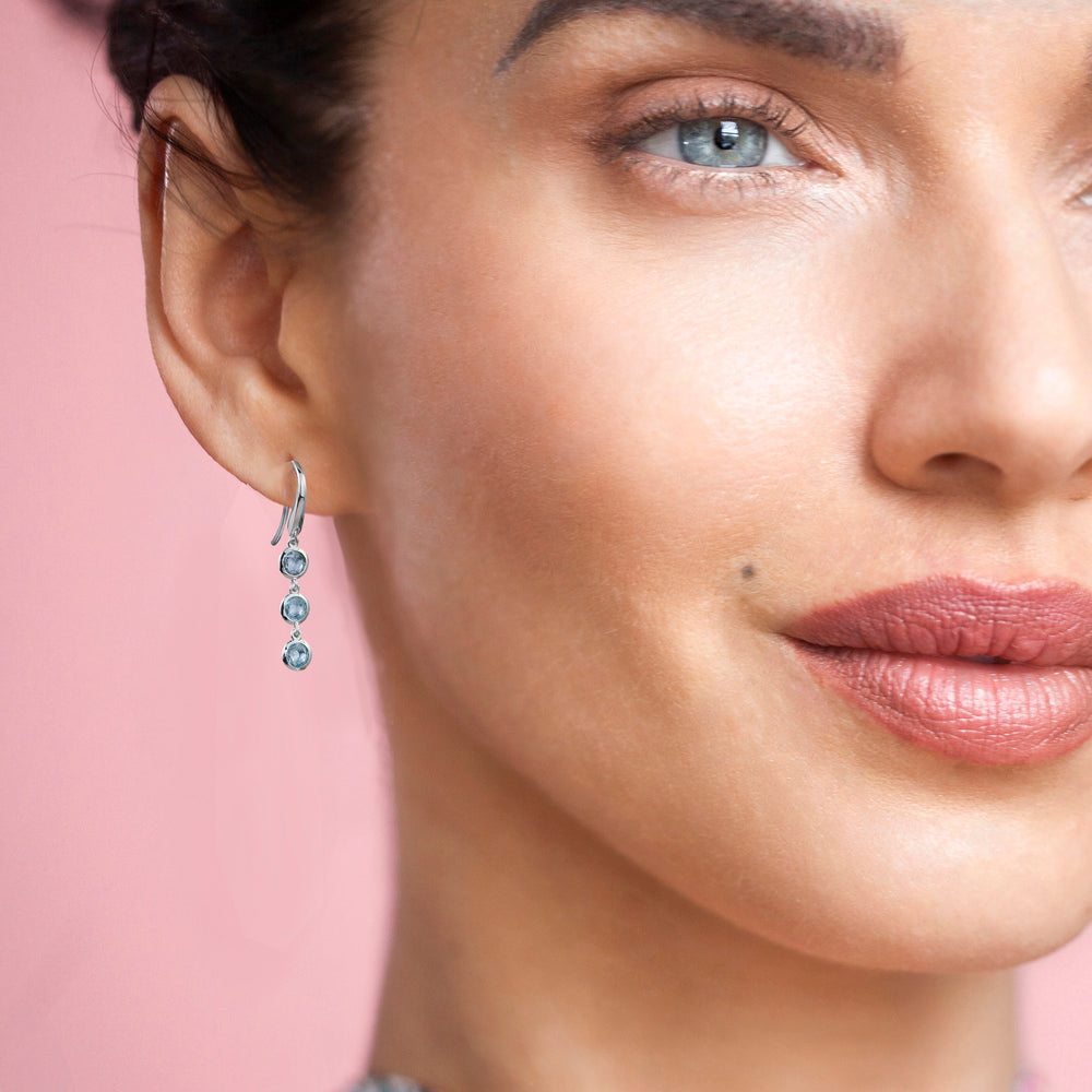 Close-up of model wearing silver drop earrings with three blue gemstones