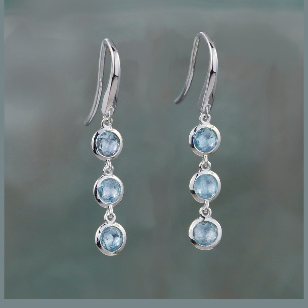 Triple stone earrings in silver with blue topaz on a gray background