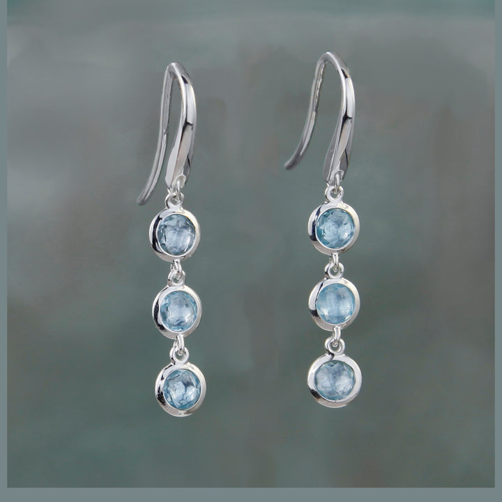 Triple stone earrings in silver with blue topaz on a gray background