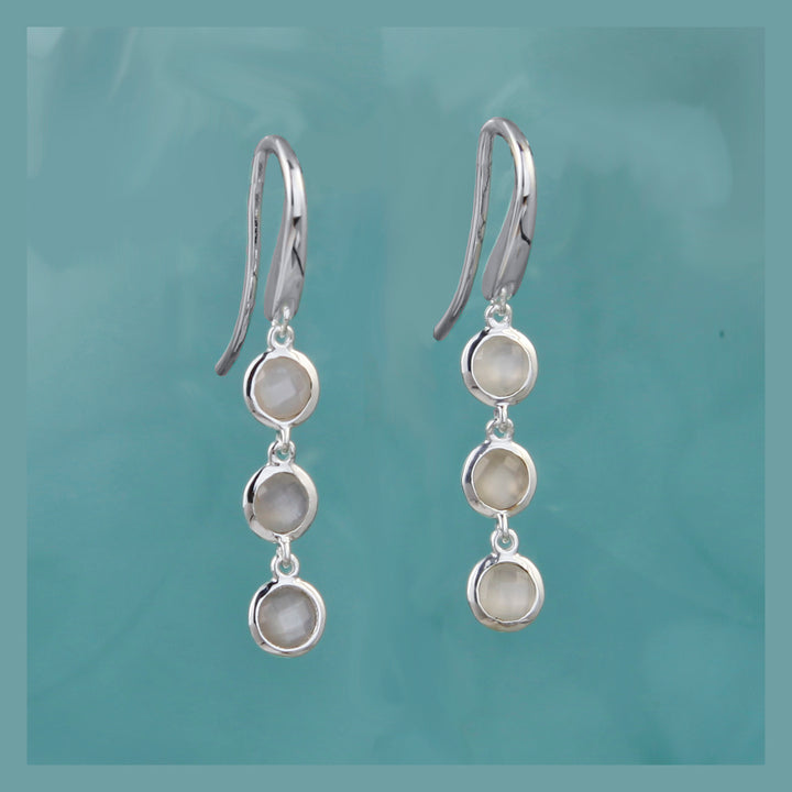 Three stone drop earrings in silver and moonstone on a aqua background