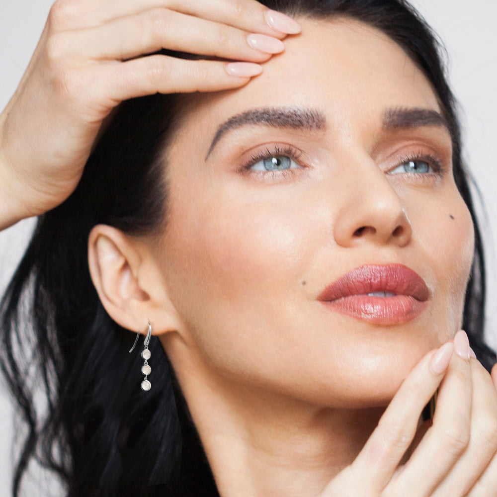 Close-up of a woman wearing silver drop earrings with three moonstone gemstones