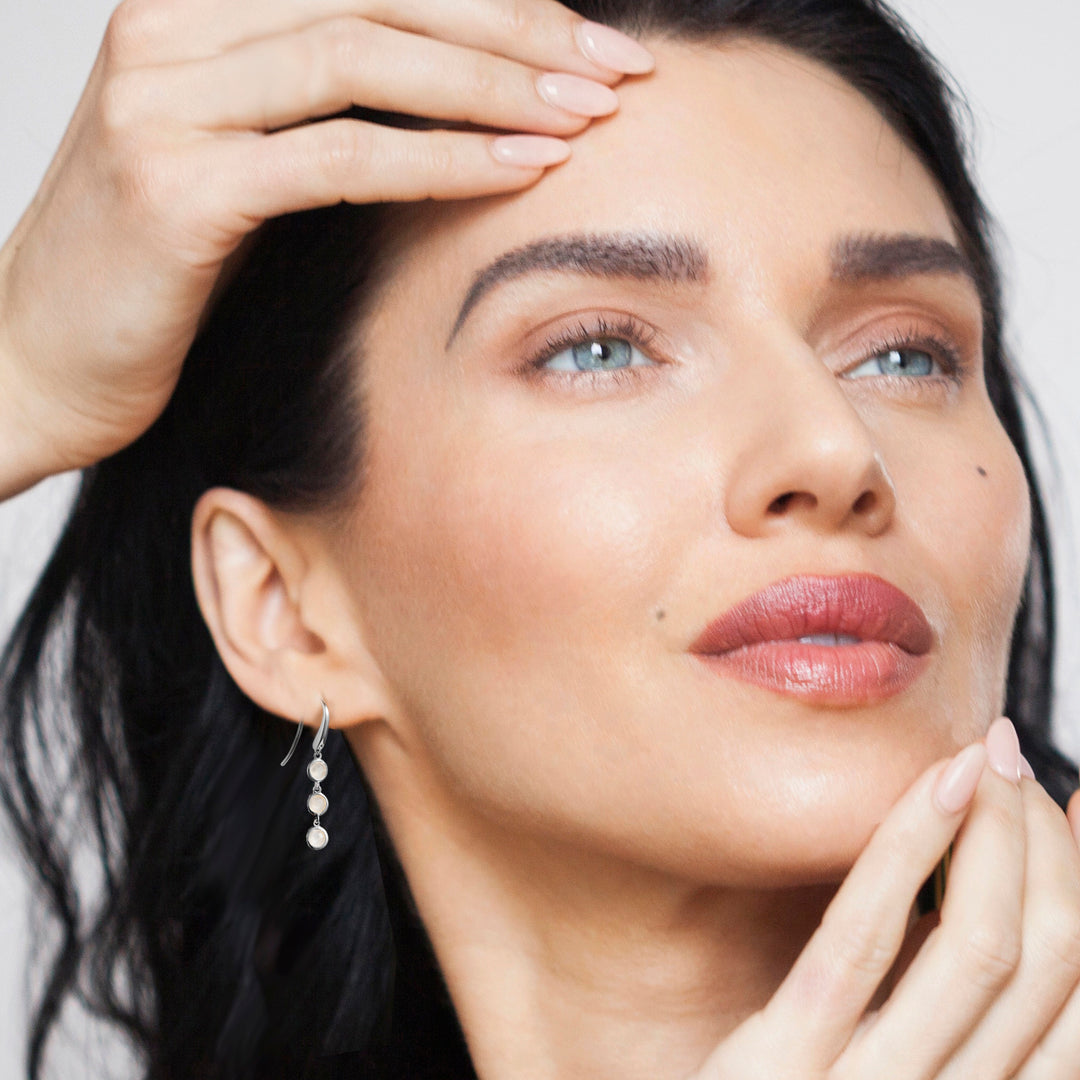 Close-up of a woman wearing silver drop earrings with three moonstone gemstones