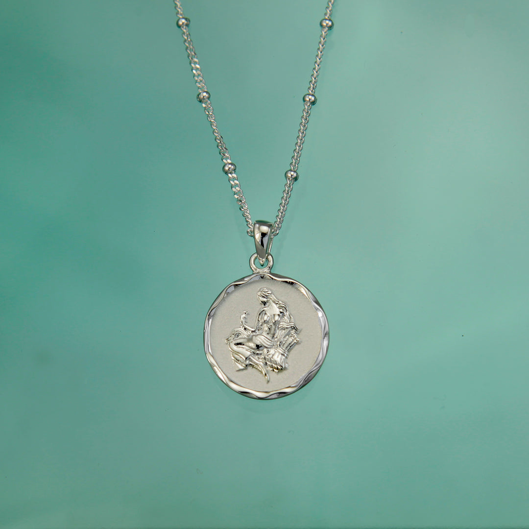 Silver virgo zodiac necklace on an aqua background