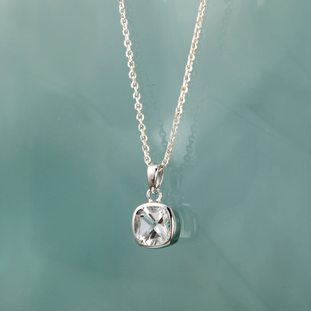 Silver necklace with a white topaz pendant on a light green background