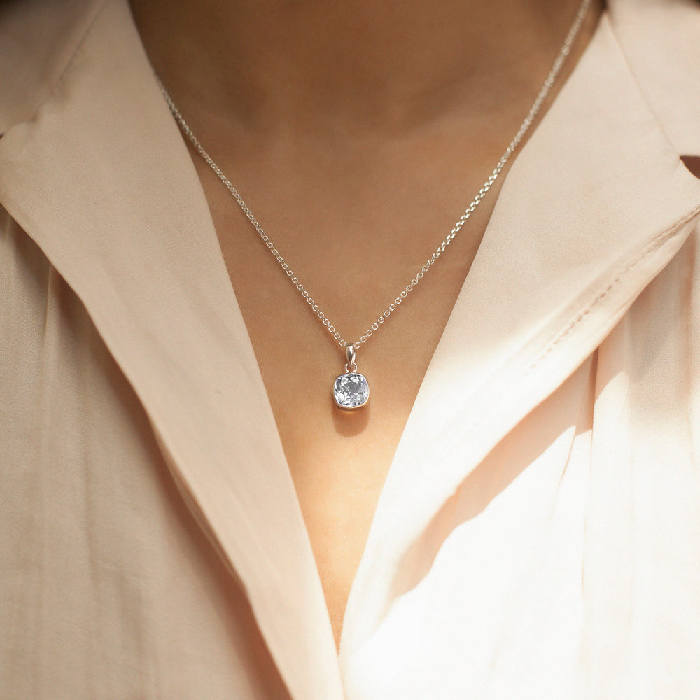 SIlver necklace with a white topaz pendant worn by a person wearing a light-colored shirt.