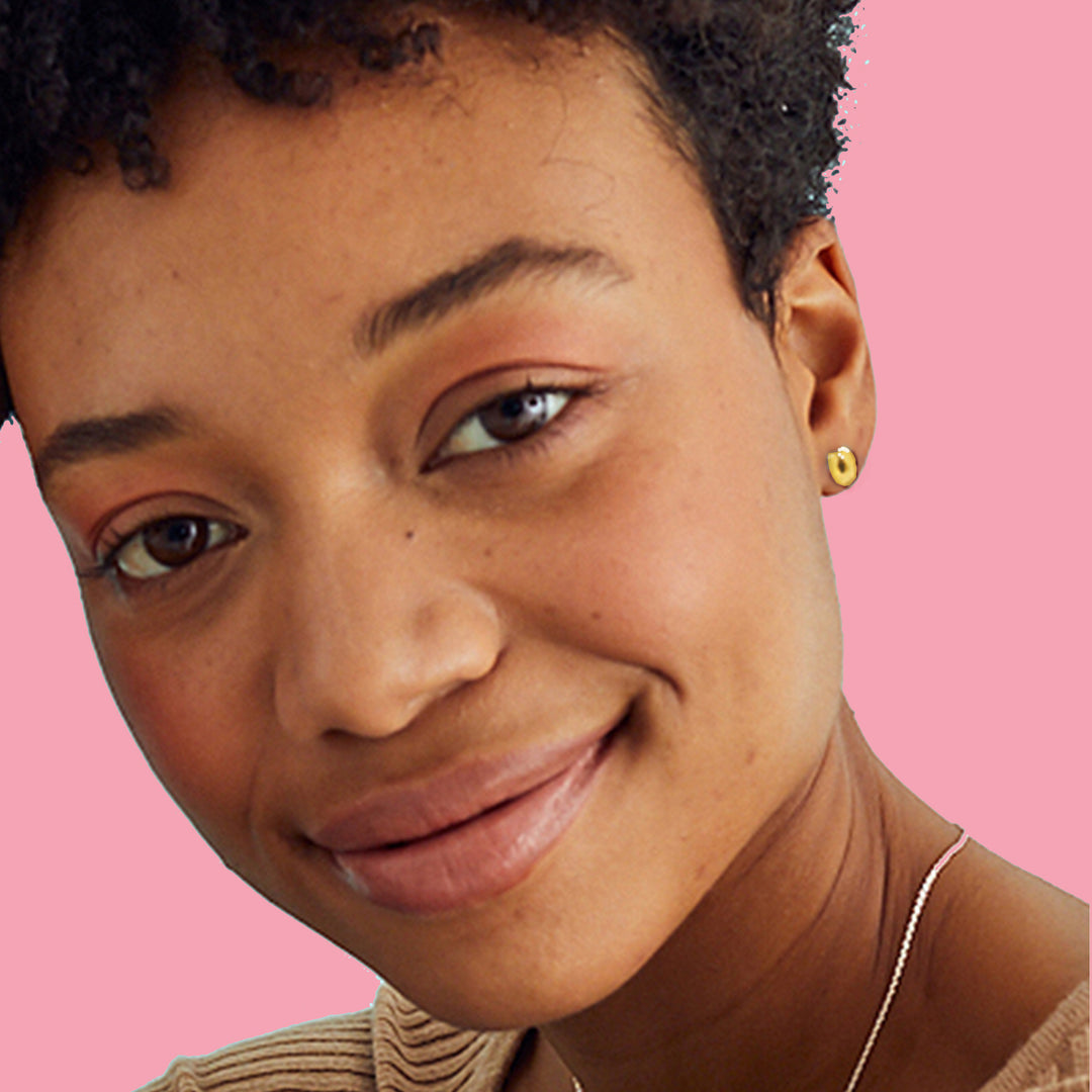 Close-up of a woman wearing gold horseshoe stud earrings on a pink background