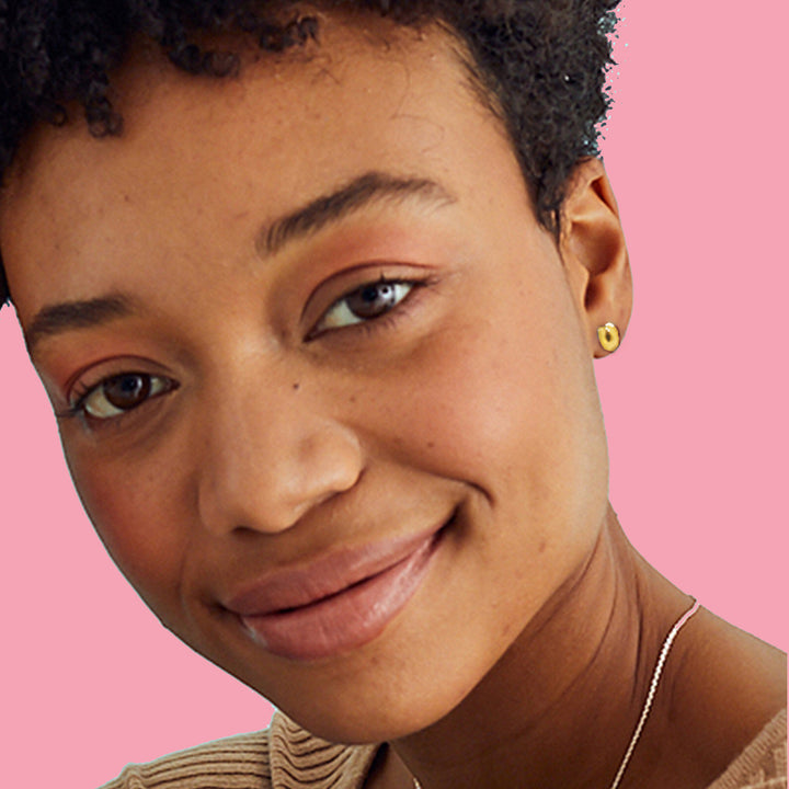 Close-up of a woman wearing gold horseshoe stud earrings on a pink background