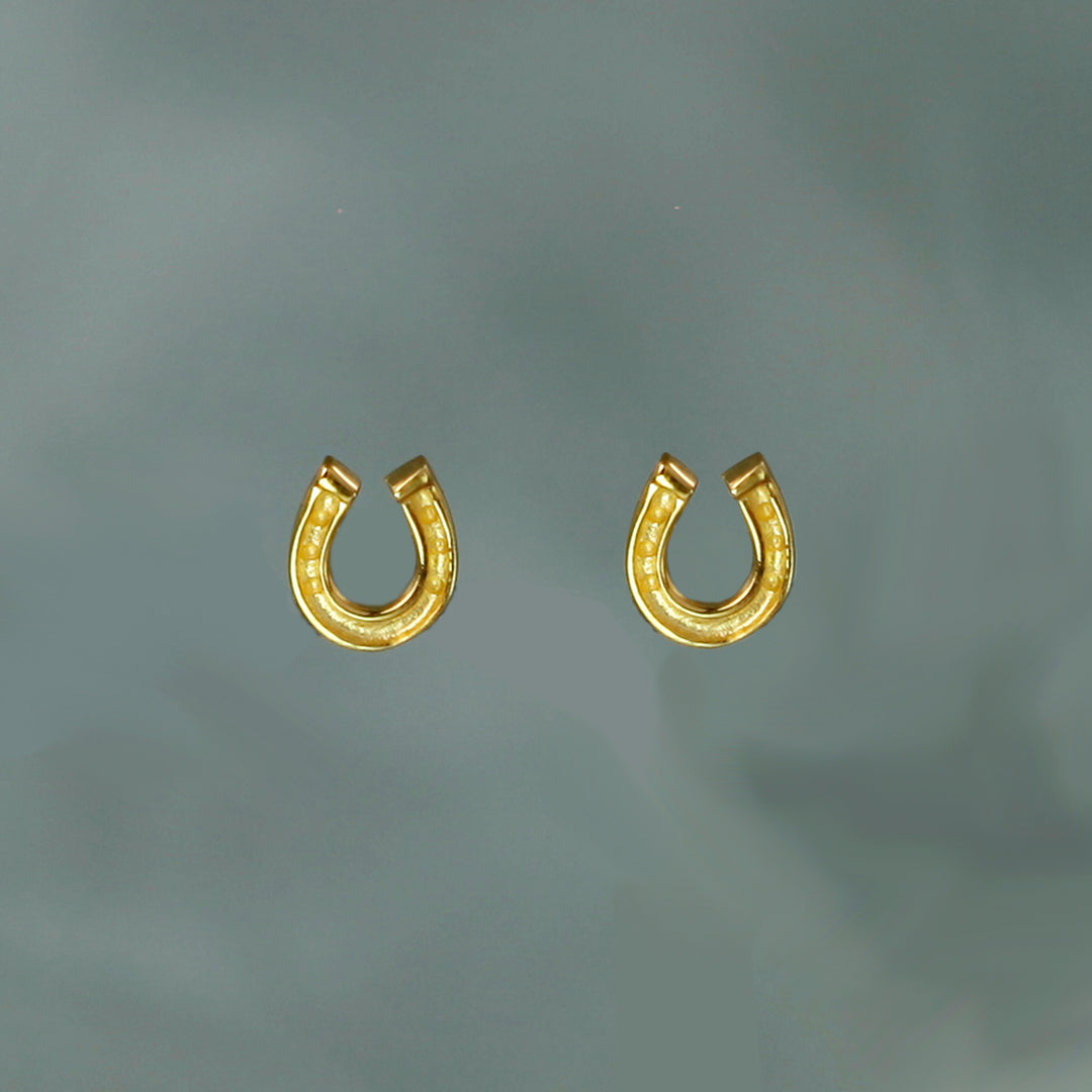 Gold horseshoe-shaped earrings on a gray background