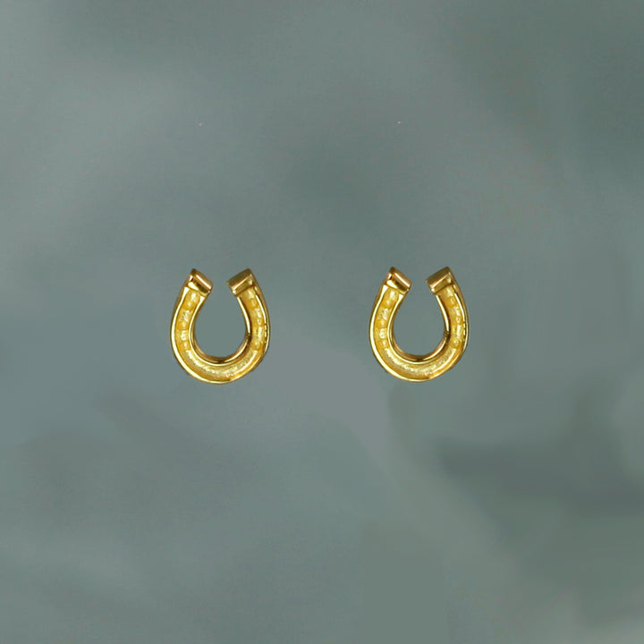 Gold horseshoe-shaped earrings on a gray background
