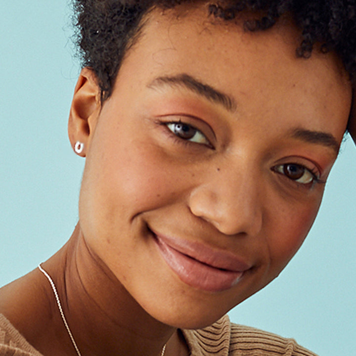 Close-up of a woman wearing silver horseshoe stud earrings on a blue background