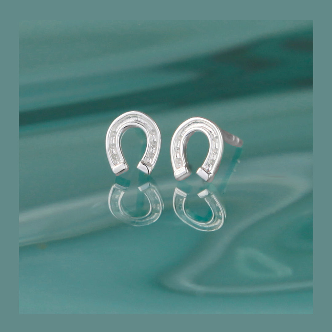 Silver horseshoe-shaped earrings on a reflective teal surface
