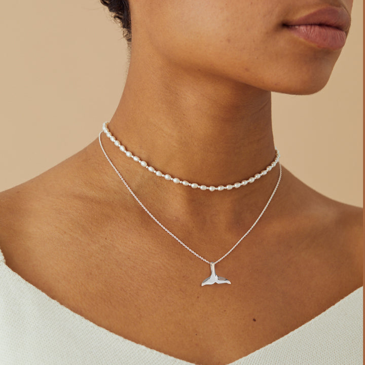 Close up of a model wearing a silver whale tail necklace and a pearl choker