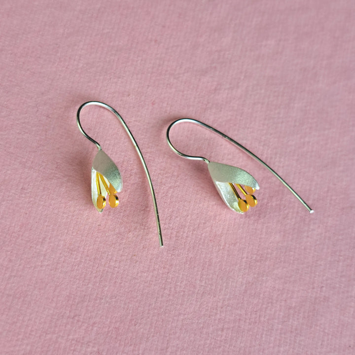 Alternative view of silver snowdrop earrings showing ear wires on a pink background.