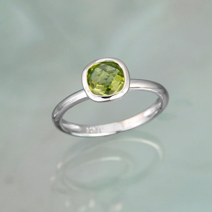 cushion cut peridot gem set in a sterling silver band on a gray background
