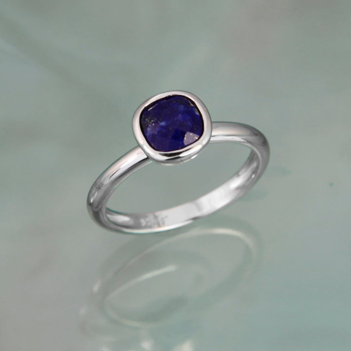 Silver solitaire ring with a dark blue gemstone on a gray background