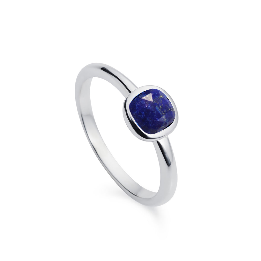 cushion cut dark blue stone set in a silver solitaire ring on a white background