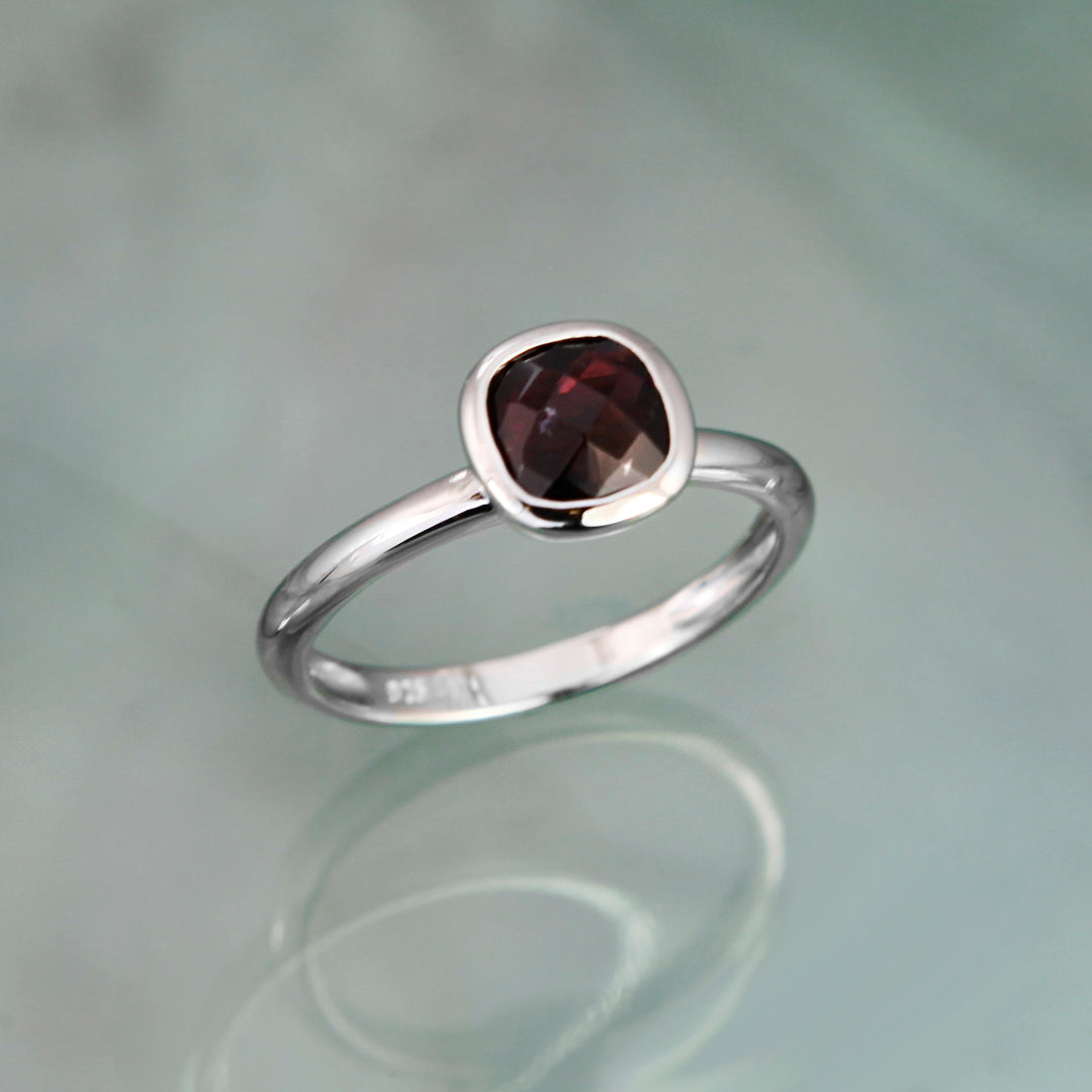 Silver ring with a square red garnet on a reflective surface