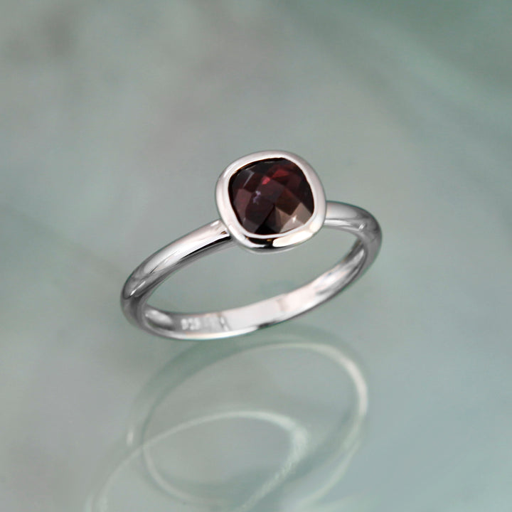 Silver ring with a square red garnet on a reflective surface
