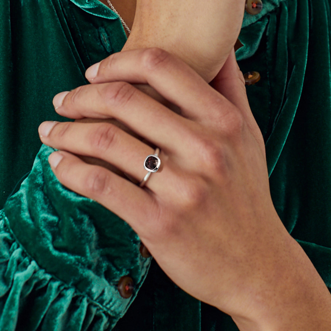 Close-up of a hand wearing a garnet ring with a green velvet garment in the background