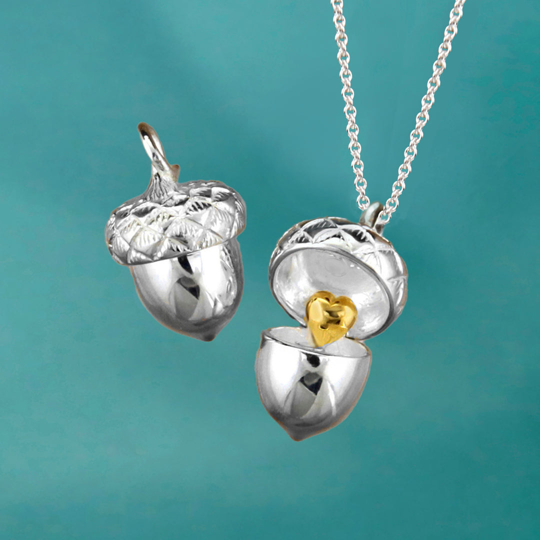 Sterling silver acorn locket necklace with gold heart detail on an aqua background