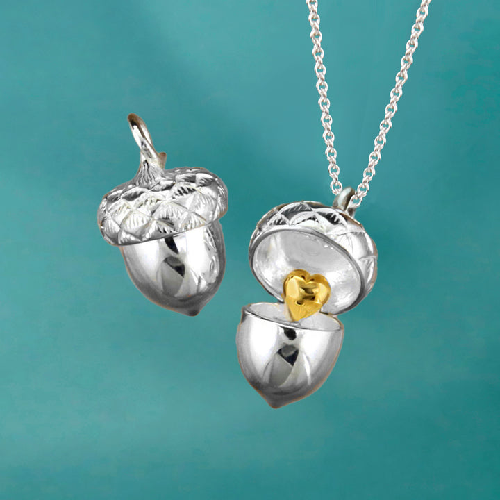 Sterling silver acorn locket necklace with gold heart detail on an aqua background