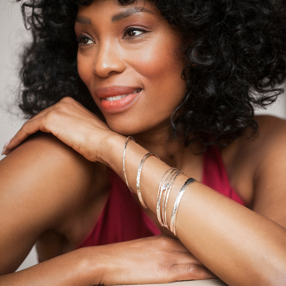 Model wearing multiple silver hammered stacking bangles.