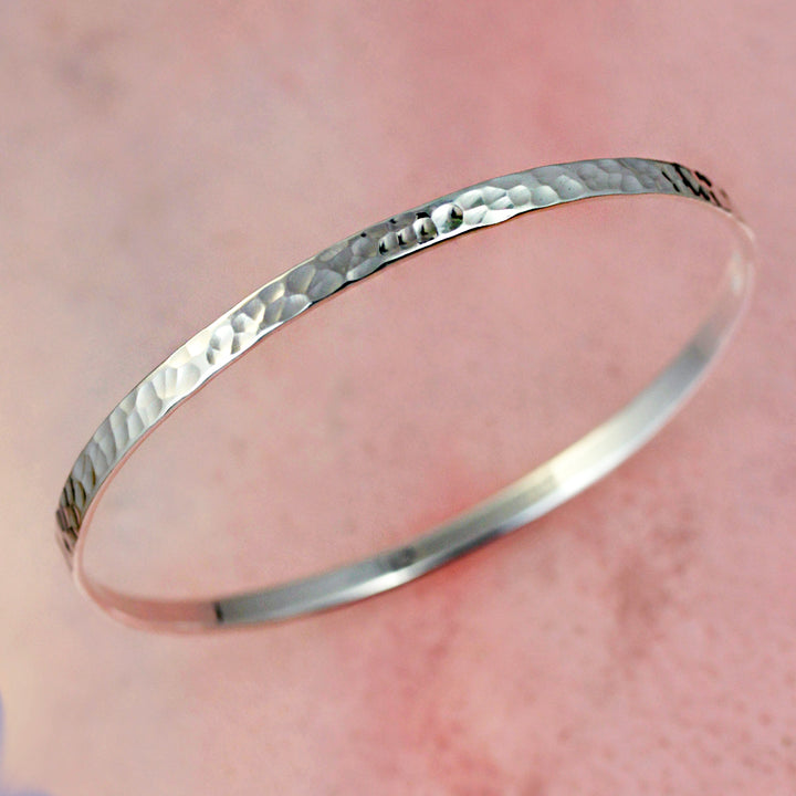 Silver hammered silver bangle bracelet on a pink background.