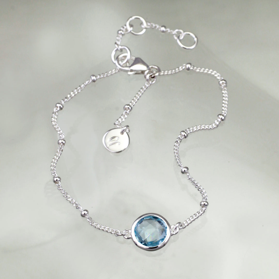 Sterling silver beaded chain bracelet with blue topaz on a reflective background