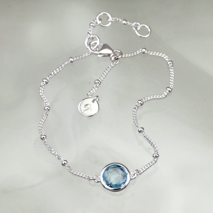 Sterling silver beaded chain bracelet with blue topaz on a reflective background