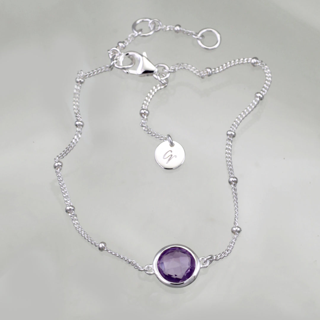 Sterling silver beaded chain bracelet with amethyst on a reflective background