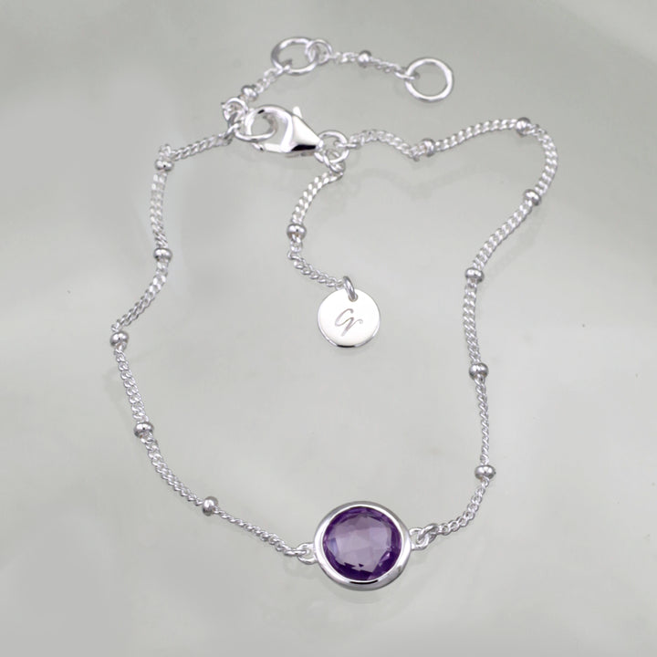 Sterling silver beaded chain bracelet with amethyst on a reflective background