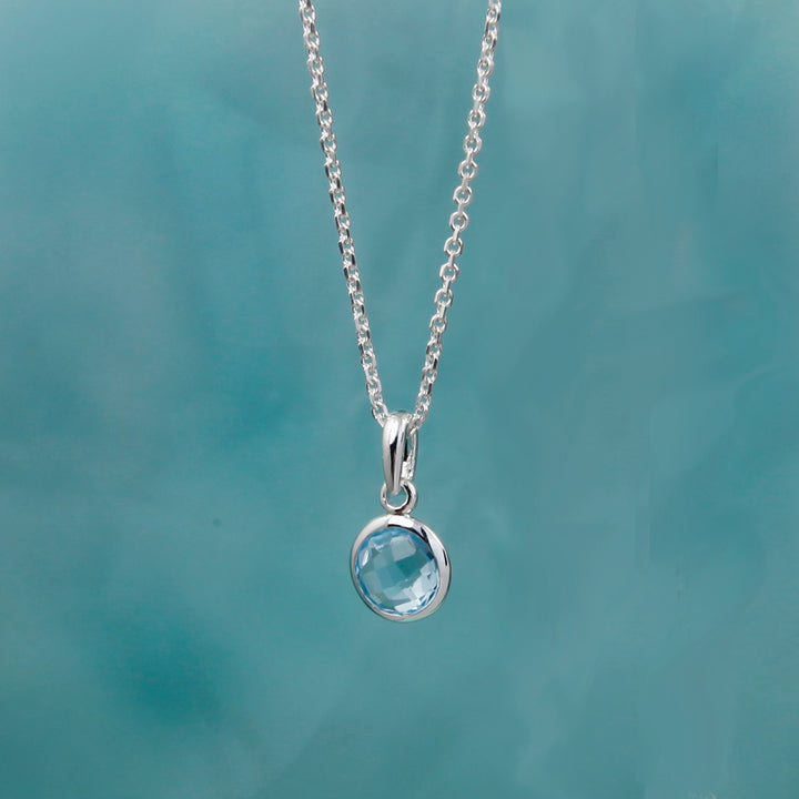 Silver pendant with a blue topaz gemstone against a teal background