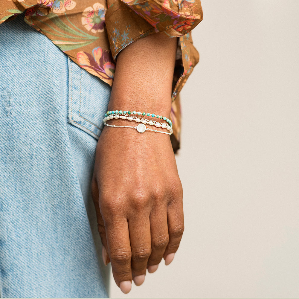 Woman wearing sterling silver beaded compass bracelet in turquoise styled with stacking bracelets