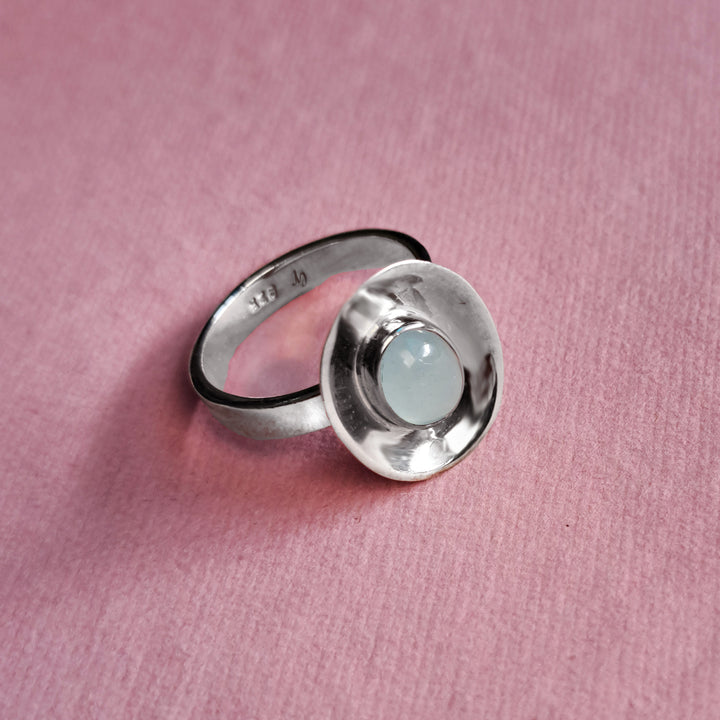 Sterling silver dish shaped ring with aquamarine cabochon gemstone on ap pink background